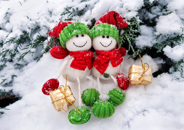 Декоративная рождественская и новогодняя композиция смешных двух снеговиков в шляпах и шарфах с подарками, сидящими в снегу. Рождественский пейзаж
. - Фото, изображение