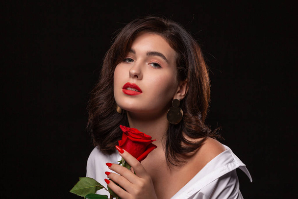 Beautiful woman with bright makeup posing isolated over black background with red rose. - Фото, изображение