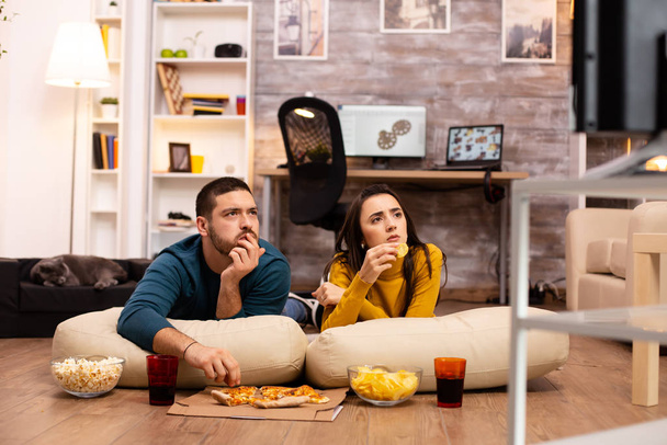 Couple sitting on the floor and watching TV in their living room - Photo, Image