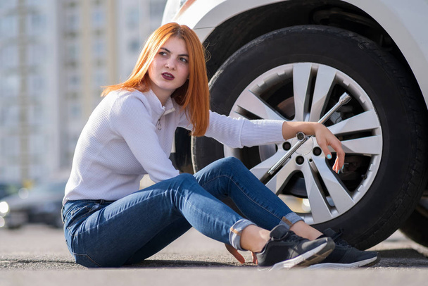 Young woman with wrench waiting for help to change wheel on a br - 写真・画像