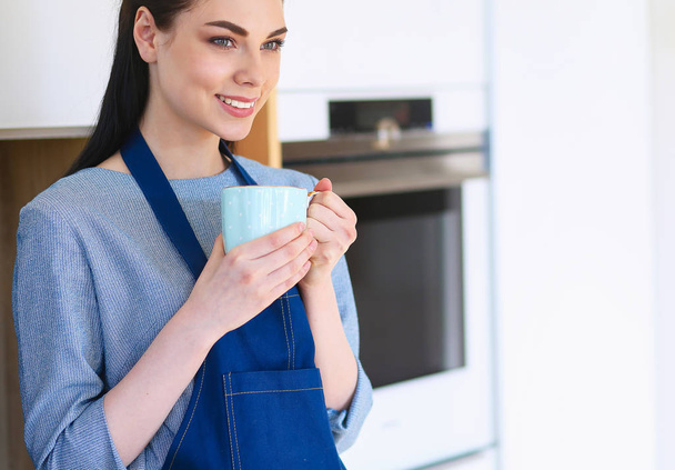 Portrait of young woman with cup against kitchen interior background - Foto, Bild