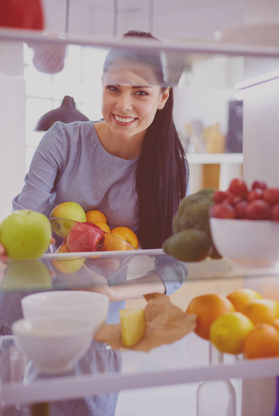Smiling woman taking a fresh fruit out of the fridge, healthy food concept - Fotoğraf, Görsel