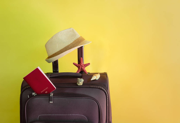 Bruine koffer, paspoort, zeesterren, schelpen en hoed op gele achtergrond. Strand vakantie concept.  - Foto, afbeelding