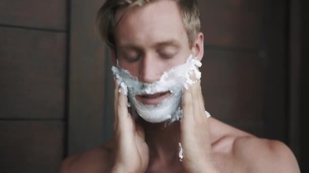 Portrait of man puts shaving foam on his face. - Кадры, видео