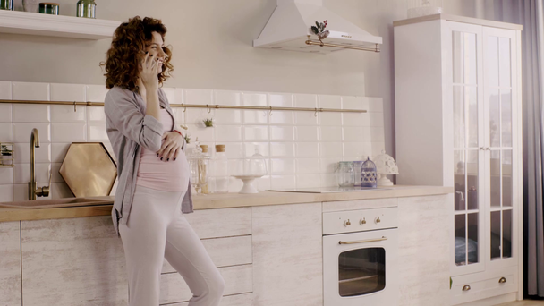 těhotná žena mluví na smartphone a dotýká břicho v kuchyni - Záběry, video