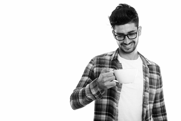 Stúdió lövés boldog perzsa fiatalember mosolyogva, miközben a gazdaság, és nézett csésze kávé - Fotó, kép