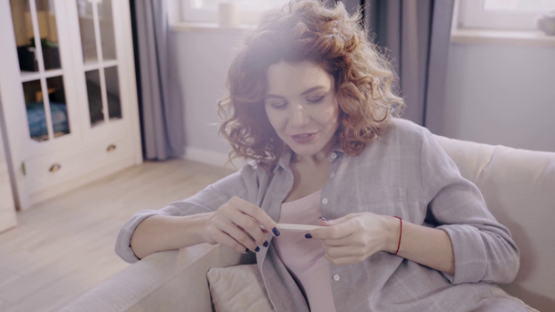 szczęśliwa kobieta w ciąży patrząc na test ciążowy na kanapie - Materiał filmowy, wideo