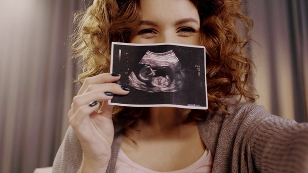 happy pregnant woman showing fetal ultrasound image at camera - Footage, Video