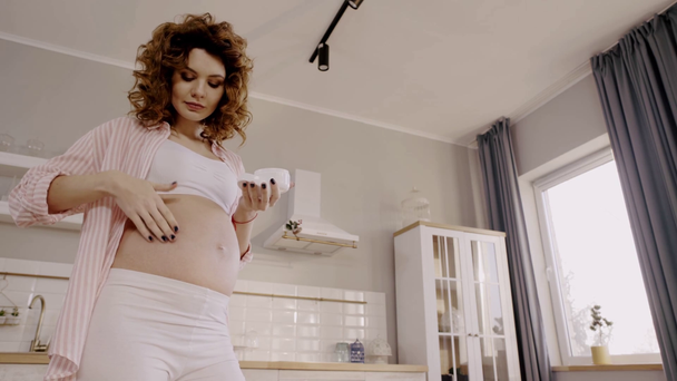 Низкий угол зрения беременной женщины при нанесении растяжки крем для живота
 - Кадры, видео