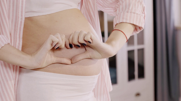 oříznutý pohled těhotné ženy ukazující srdeční gesto na bříšku - Záběry, video