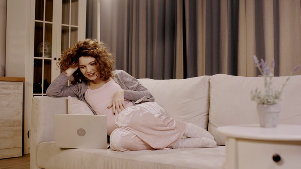 mujer embarazada feliz viendo la película en el ordenador portátil y tocando el vientre en el sofá
 - Metraje, vídeo