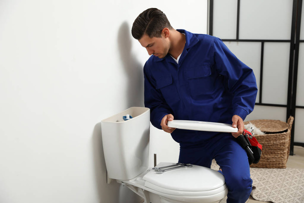 Professional plumber working with toilet bowl in bathroom - Foto, afbeelding