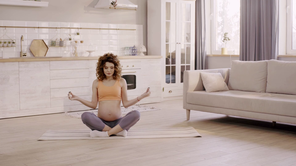 pregnant woman meditating in lotus pose at home on yoga mat - Filmati, video