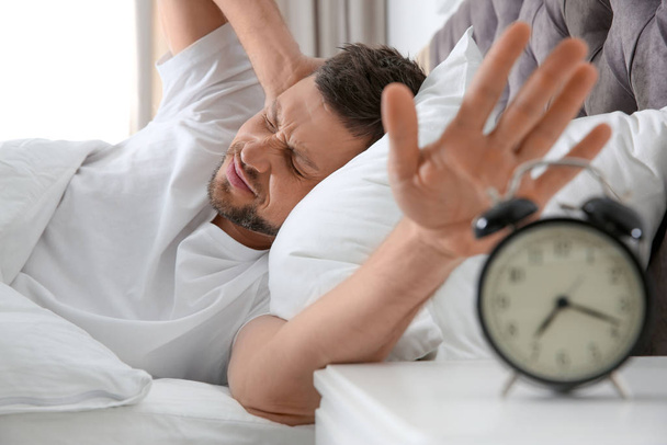 Sleepy man turning off alarm clock at home in morning - Foto, Bild