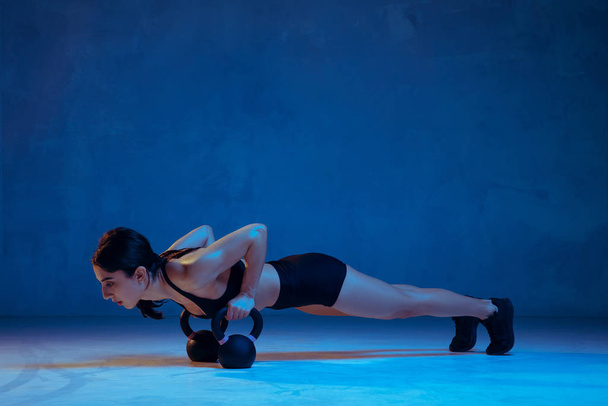 Caucasian young female athlete practicing on blue studio background in neon light - Valokuva, kuva