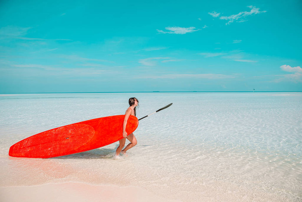 Beautiful surfer woman ready to surfing in turquoise sea, on stand up paddle board at exotic vacation - Photo, Image