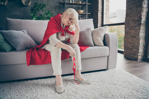 Portrait of her she nice attractive tired sick ill gray-haired blonde grandma wearing red costume sitting on divan after rescue planet at industrial brick loft modern style interior house flat - Foto, imagen