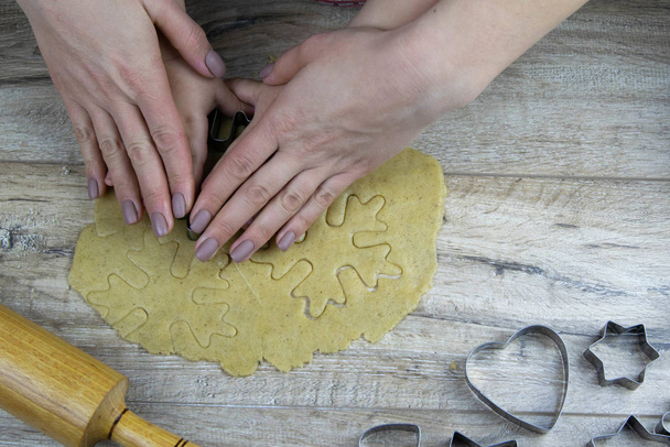 A child handstake out ginger cookies from rolled dough, cutter form a fir on a dark wooden background. - Fotoğraf, Görsel