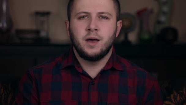 A young guy of European appearance sits in a chair in a plaid shirt mouth warm up, rehearsing a speech before recording a vlog - Séquence, vidéo
