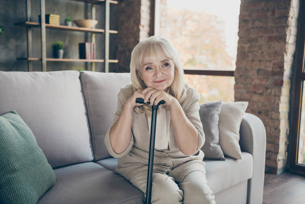 Photo of white haired aged grandma holding walking cane remembering youth light sadness romantic memories missing husband sitting divan sofa living room apartments indoors - Fotografie, Obrázek