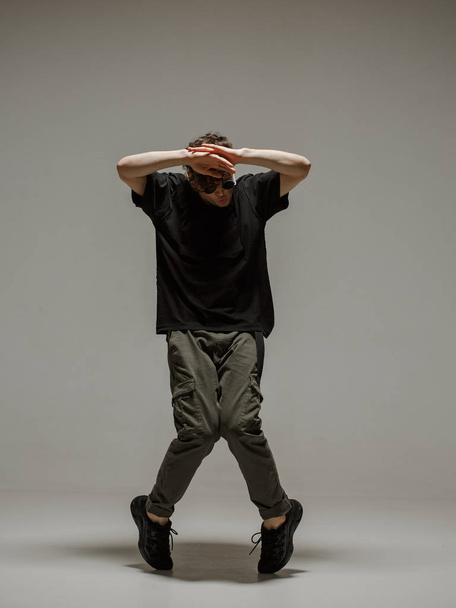 Guy dancing contemporary dance in studio. Neutral grey background. Acrobatic bboy dancer. - Foto, afbeelding