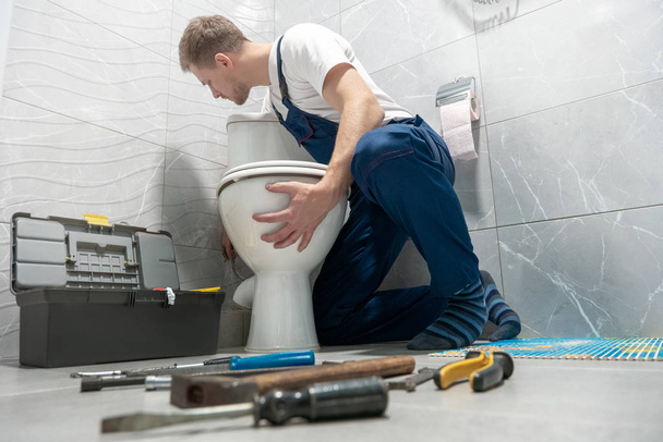 man plumber in uniform installing toilet bowl using instrument kit professional repair service - Zdjęcie, obraz