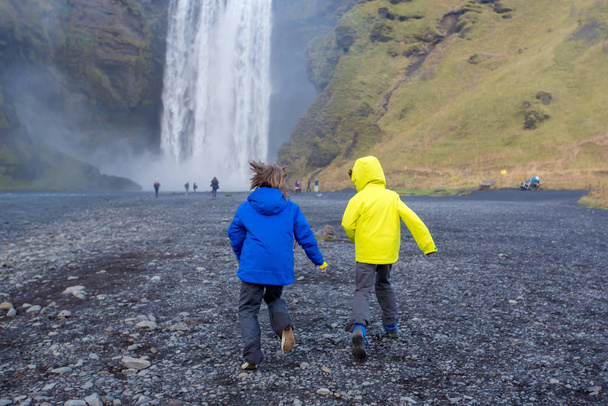 Cute child playing in front of the Skogafoss waterfall in Icelan - Fotó, kép