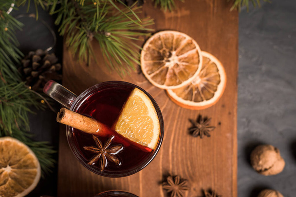 Christmas mulled wine in a transparent glass with orange slices on the basis of red wine with spicy cinnamon sticks, star anise, on a black background. - Zdjęcie, obraz