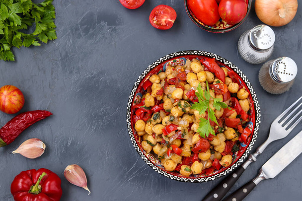 Garnierung von Kichererbsen mit Paprika und Tomaten, ein vegetarisches Gericht reich an Proteinen, auf einem Teller vor dunklem Hintergrund liegend, Nahaufnahme, Draufsicht - Foto, Bild