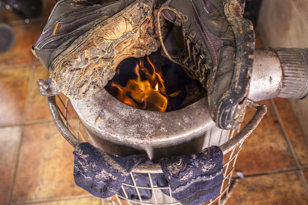 Wet used boots and socks drying over firewood stove - 写真・画像