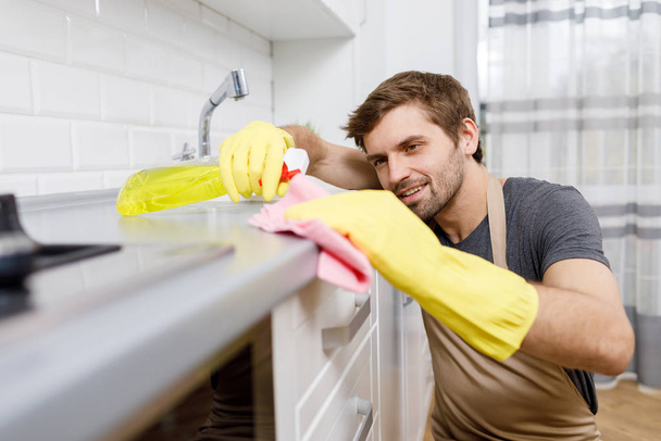 Młody mężczyzna w żółtych rękawiczkach używa środka czyszczącego - Zdjęcie, obraz