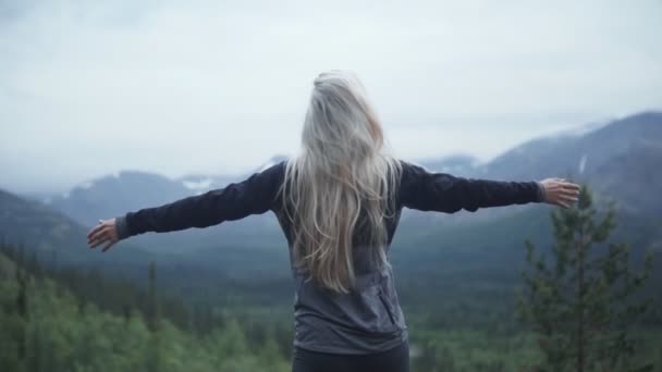 yong blond with long hair open arms at mountain peak. Girl stretch arms and relaxed at the mountain background - 映像、動画