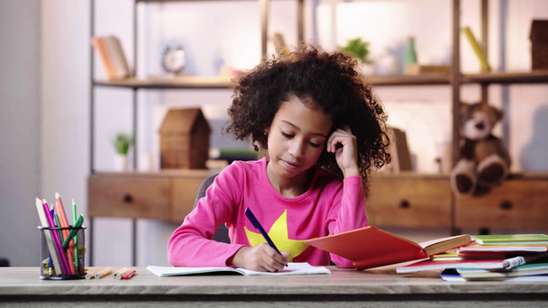 zamyšlené africké americké dítě ukazující myšlenkové gesto a psaní v copybooku - Záběry, video