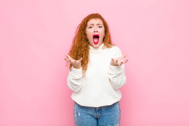 young red head woman looking desperate and frustrated, stressed, unhappy and annoyed, shouting and screaming against pink wall - 写真・画像