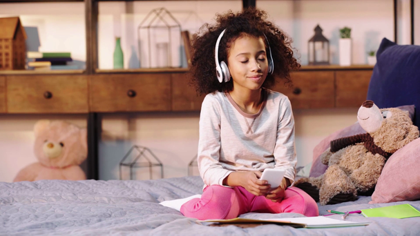 Африканский американский ребенок слушает музыку во время выполнения домашней работы в постели
 - Кадры, видео