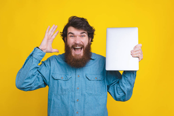 Foto di uomo hispter barbuto che tiene il nuovo computer portatile su sfondo giallo
 - Foto, immagini