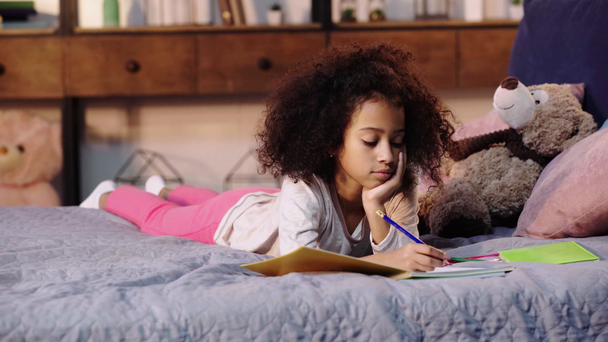 Afrikkalainen amerikkalainen lapsi tekee läksyjä sängyssä lähellä nallekarhu
 - Materiaali, video