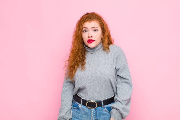 young red head woman feeling clueless, confused and uncertain about which option to pick, trying to solve the problem against pink wall - Foto, Imagem