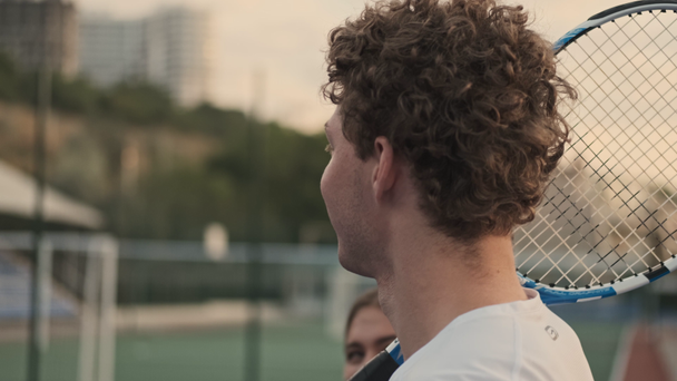 Widok z boku wesoły kręcone samiec tenisista trzyma rakietę tenisową i spaceru z jego przeciwniczką na korcie tenisowym - Materiał filmowy, wideo