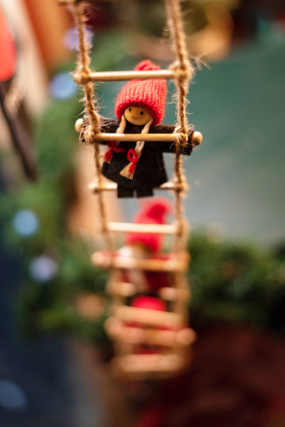 Little cute rag doll climbing the rope ladder. Little gnome dolls in red hats sitting on Christmas stairs. Christmas decoration. Selective focus - Photo, Image