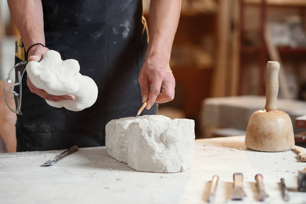 Male hands working with a white stone. Professional sculptor carves stone sculpture from limestone. - Фото, зображення