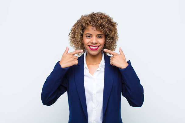 young woman african american smiling confidently pointing to own broad smile, positive, relaxed, satisfied attitude against flat wall - Foto, afbeelding
