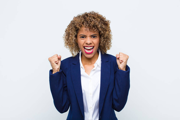 young woman african american feeling happy, surprised and proud, shouting and celebrating success with a big smile against flat wall - Foto, afbeelding