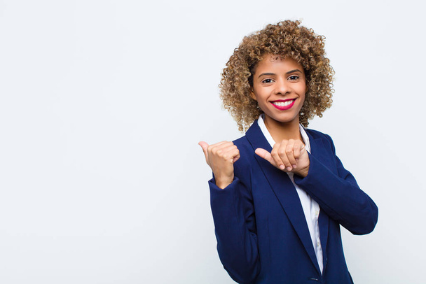 young woman african american smiling cheerfully and casually pointing to copy space on the side, feeling happy and satisfied against flat wall - Foto, Imagem