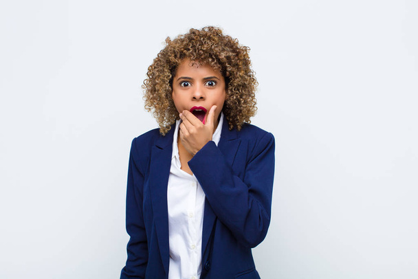 young woman african american with mouth and eyes wide open and hand on chin, feeling unpleasantly shocked, saying what or wow against flat wall - Foto, imagen