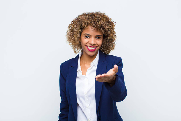 young woman african american smiling, looking happy, confident and friendly, offering a handshake to close a deal, cooperating against flat wall - Foto, Imagen
