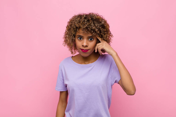 young african american woman feeling confused and puzzled, showing you are insane, crazy or out of your mind against pink wall - Fotoğraf, Görsel