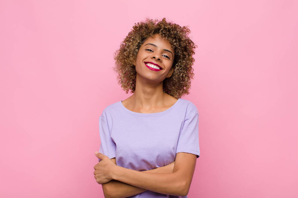 young african american woman laughing happily with arms crossed, with a relaxed, positive and satisfied pose against pink wall - Fotografie, Obrázek