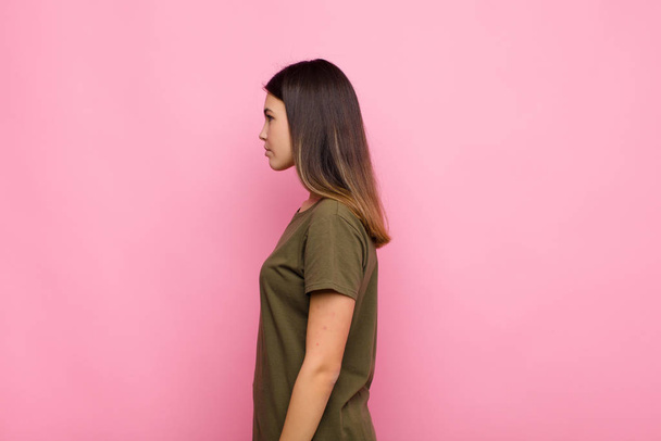 young pretty woman on profile view looking to copy space ahead, thinking, imagining or daydreaming against pink wall - Fotoğraf, Görsel