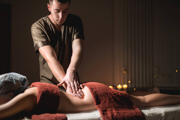 Professionele premium massage in een donkere atmosferische kast. Jongeman doet massage aan een vrouwelijke cliënt in een donker kantoor op de achtergrond van brandende kaarsen - Foto, afbeelding